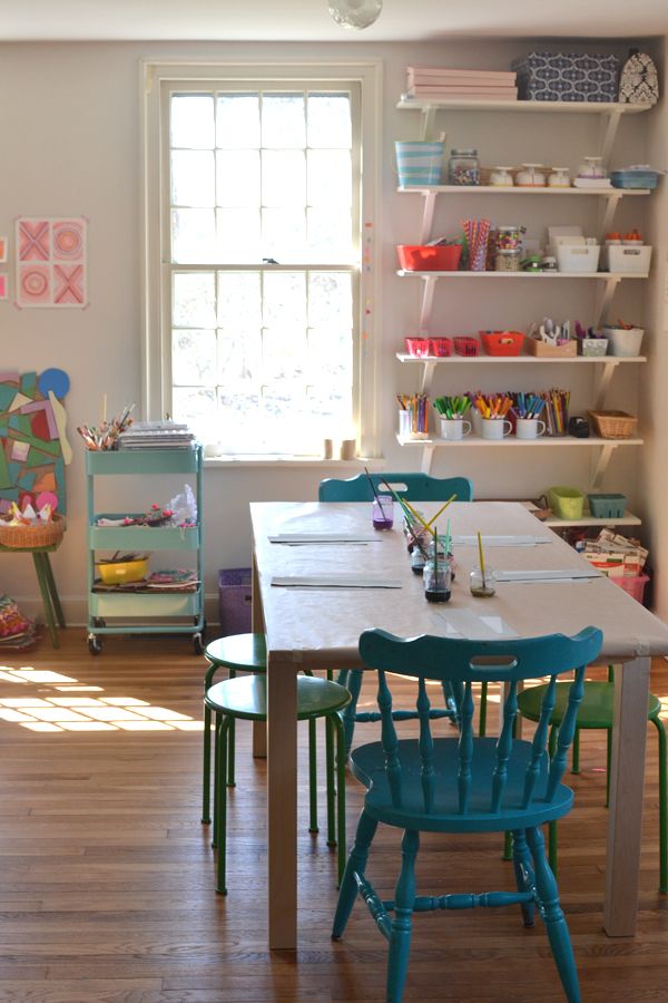 a table and chairs in a room with shelves on the wall behind it, and an open window