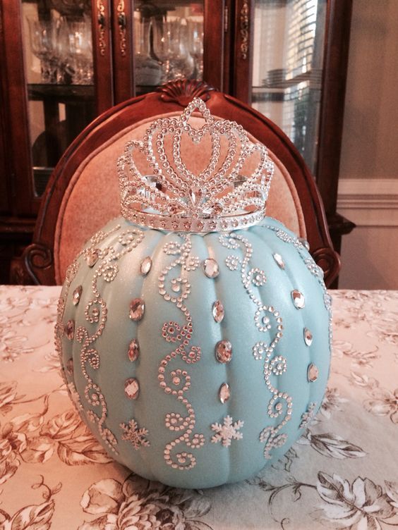 a blue pumpkin with a tiara on top sitting on a table in front of a china cabinet