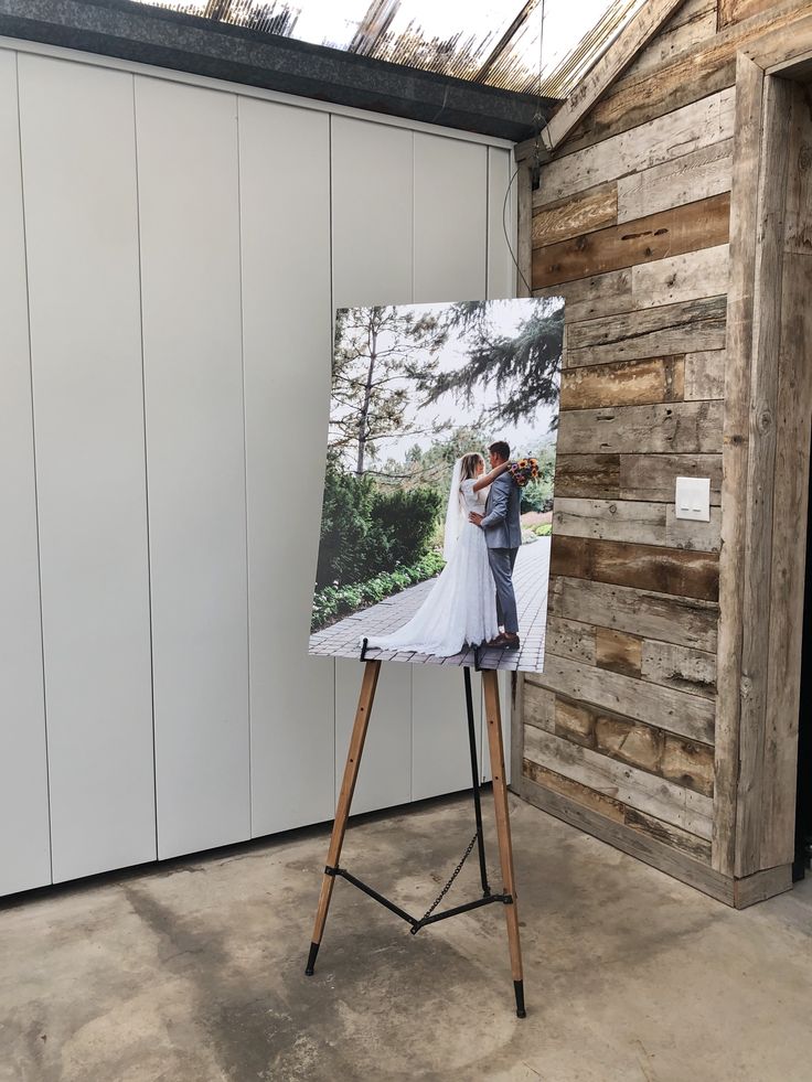 an easel with a wedding photo on it in front of a wooden wall and door