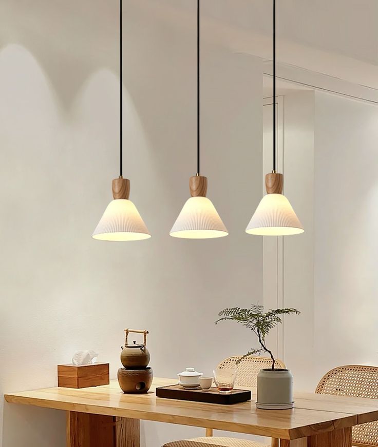 three lights hanging from the ceiling above a table with chairs and a potted plant