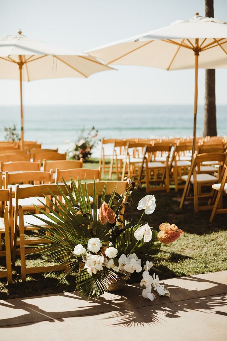 chairs and umbrellas set up on the lawn for an outdoor wedding ceremony by the ocean