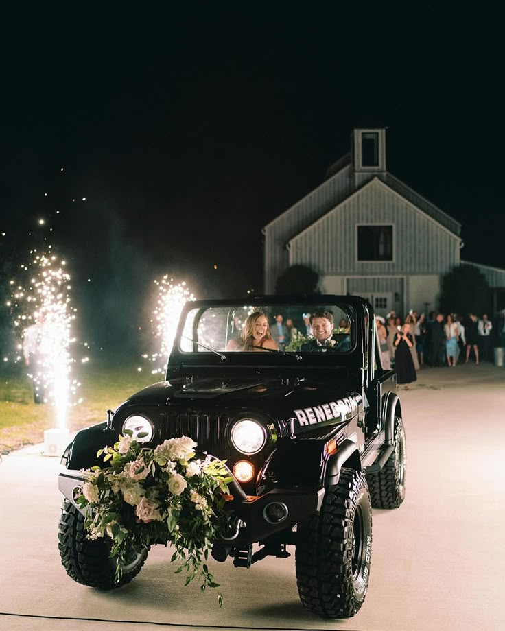 a jeep driving down a street with people in the back seat and fireworks behind it