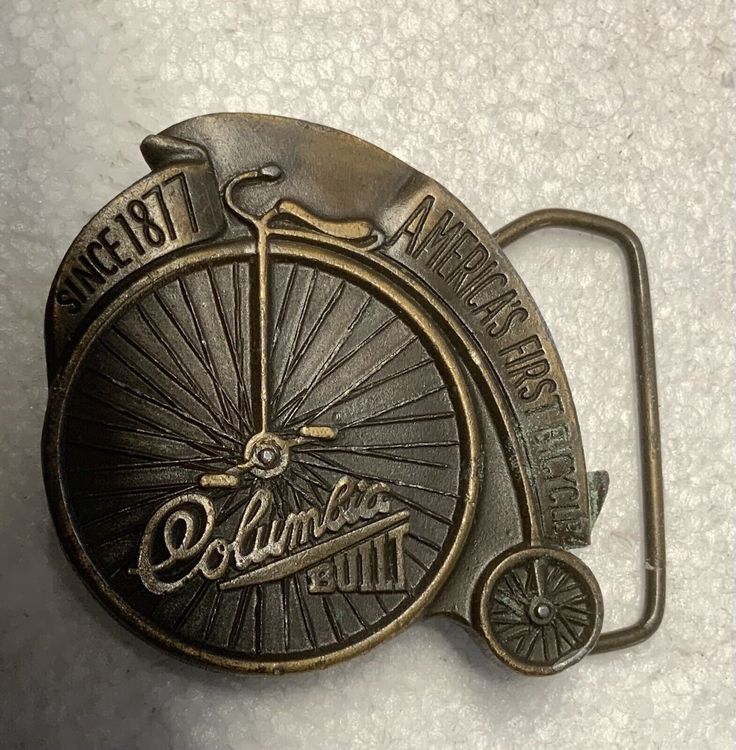 This vintage belt buckle is a must-have for any collector or fan of cycling. Featuring a solid pattern and brass plating, this piece from Bergamot Brass Works is a true vintage item from the 1970s. Measuring 2.40"(w) x 2.50"(h) and fitting belts up to 1.90" in width, it is perfect for both men and women.  The unique TF05112 ID confirms the authenticity of this classic piece, which celebrates the history of the Columbia bicycle brand. Made in the United States, this belt buckle is a great additio Vintage Brass Buckle Belt Buckles Collectible, Vintage Gold Belt Buckles For Collectors, Vintage Adjustable Belt Buckles With Brass Buckle, Bicycle Brands, Vintage Belt Buckles, Vintage Belt, Suspender Belt, The 1970s, Solid Pattern