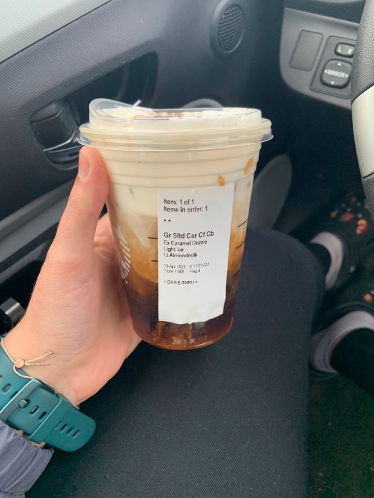 a person holding up a cup of iced coffee in their hand while sitting in the driver's seat of a car