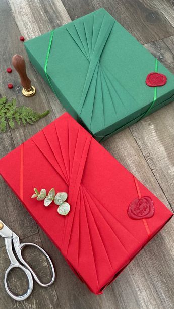 two green and red gift boxes sitting on top of a wooden floor next to scissors