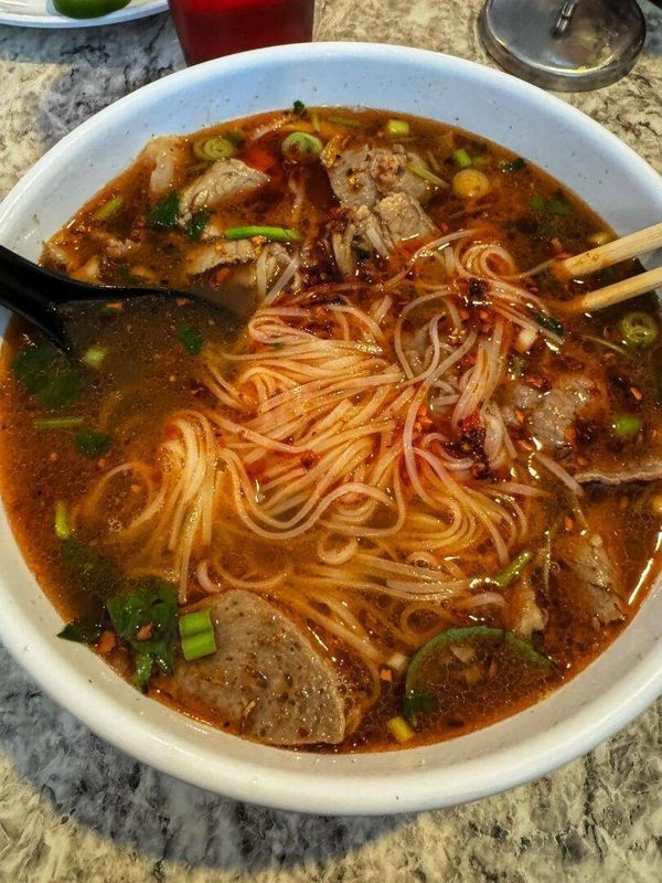 a bowl of noodles and meat soup with chopsticks