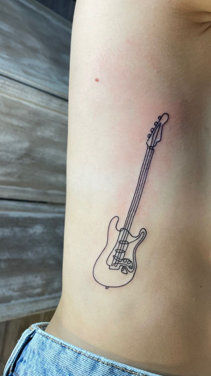 a woman's stomach with a small guitar tattoo on her left side ribcage