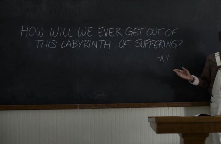 a man standing in front of a blackboard with writing on it and someone holding his hands out