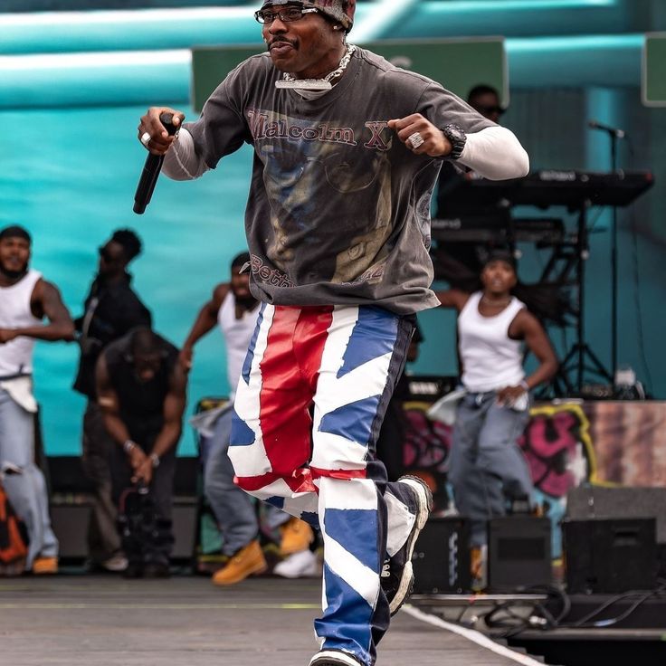 a man in an american flag pants and hat is performing on stage with other people behind him