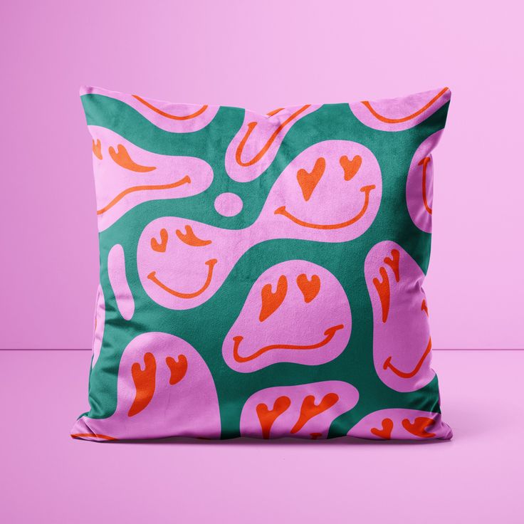 a pink and green pillow with hearts on it sitting against a pink wallpaper background