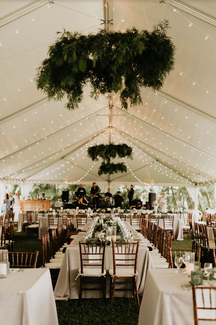 tables and chairs are set up in a tent for an outdoor wedding reception with greenery hanging from the ceiling