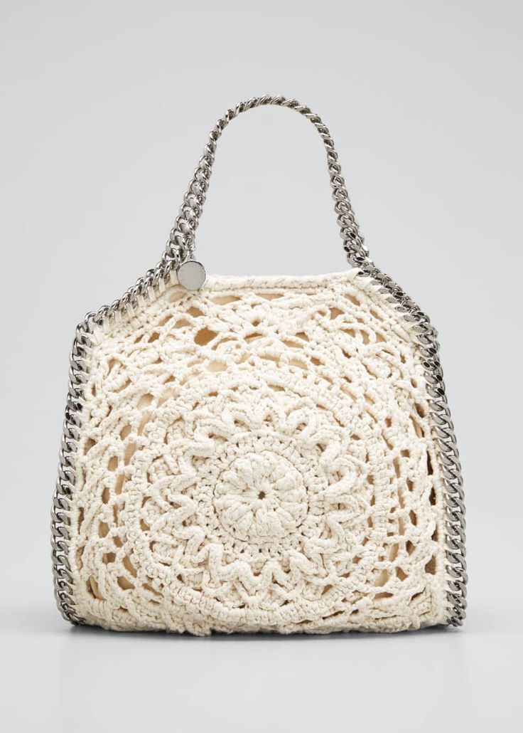 a white handbag with chain handles and an intricate crochet design on the front