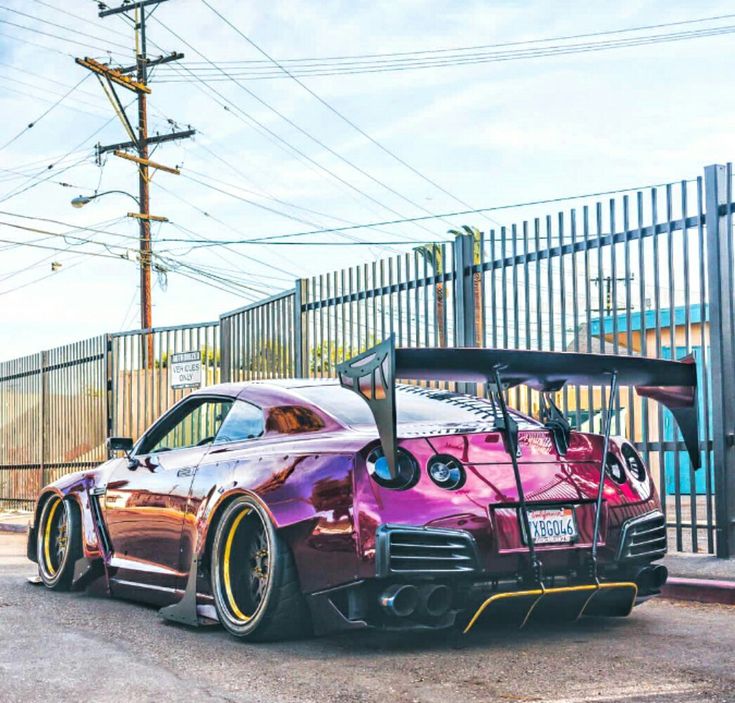 a purple sports car parked on the side of the road next to a metal fence