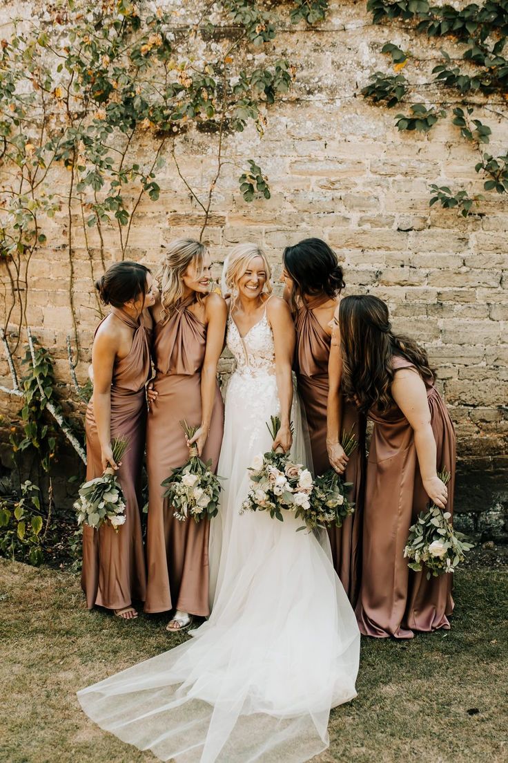 a group of women standing next to each other in front of a brick wall with greenery