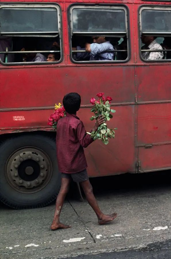 a person walking by a red bus with flowers in it's hand and people on the other side