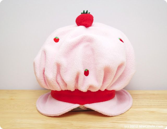 a pink hat with strawberries on it sitting on top of a wooden table next to a white wall