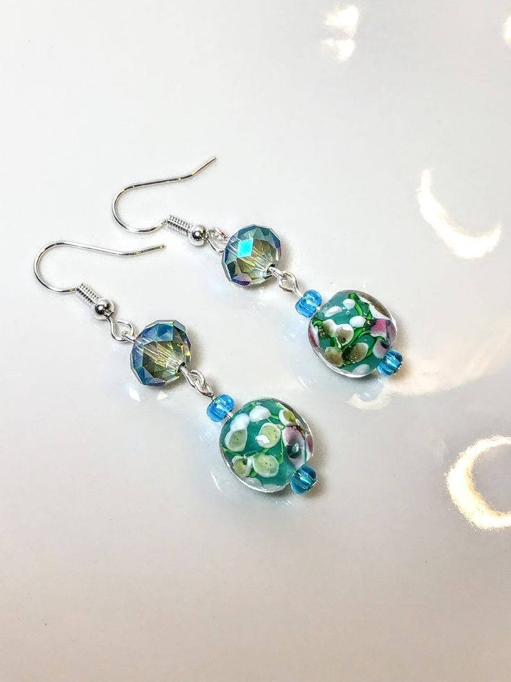 a pair of blue and green glass beaded earrings on a white plate with silver earwires