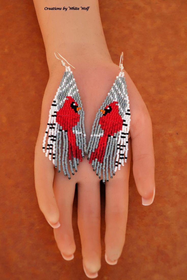 a person's hand with beaded red bird earrings on top of their palm