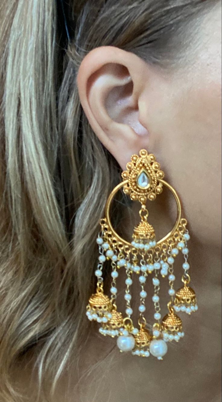 The Nila Earrings are a dazzling showstopper with intricate deep gold detailing and a kundan gemstone flower. Their enchanting design, inspired by sun showers, features delicate gold threads and ornate bells. 22k Gold Teardrop Jewelry For Wedding, Yellow Gold Jhumkas With Latkans For Wedding, Festive 22k Yellow Gold Chandelier Earrings, Festive Yellow Gold Jhumkas For Diwali, Traditional Yellow Gold Chandbali Chandelier Earrings, Festive Yellow Gold Bollywood Danglers, Brass Chandbali Bridal Earrings, Yellow Gold Chandbali Earrings With Intricate Design, 22k Gold Chandbali Bridal Earrings With Latkans