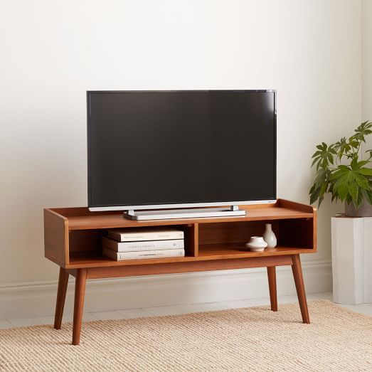 a flat screen tv sitting on top of a wooden stand next to a potted plant