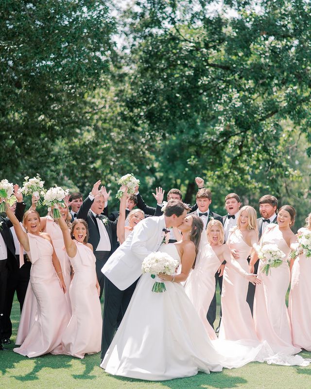 a large group of people in formal wear posing for a photo with their hands up