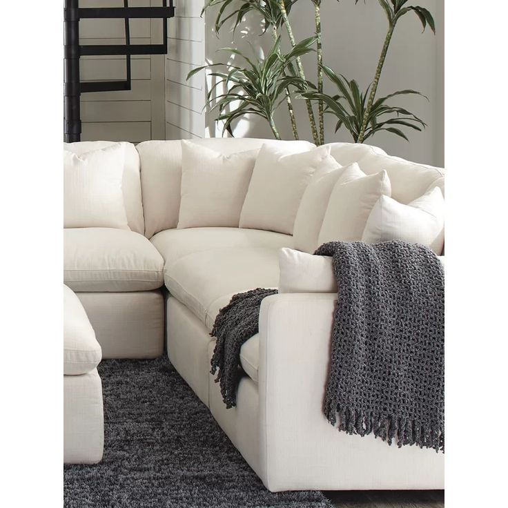 a living room with a large white sectional couch and pillows on the floor next to a plant