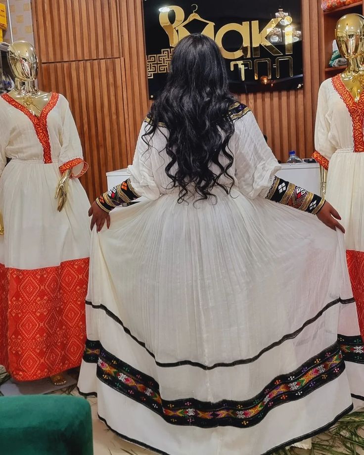 a woman standing in front of three mannequins wearing white and orange dresses