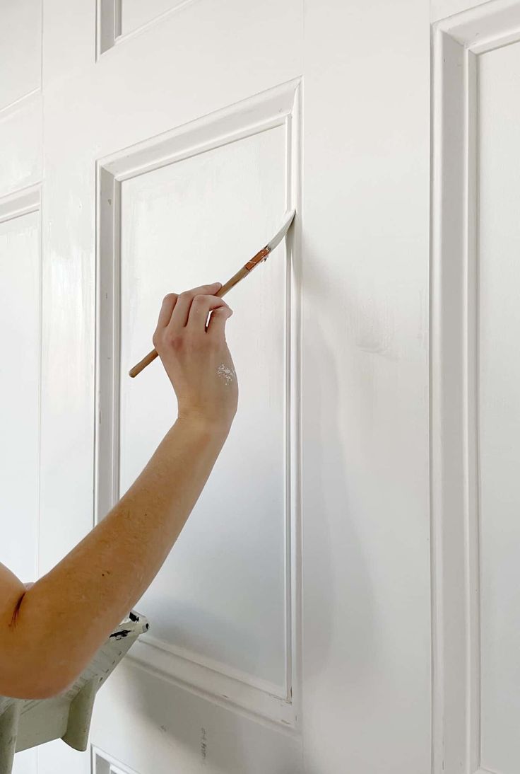 a woman is painting the wall with white paint