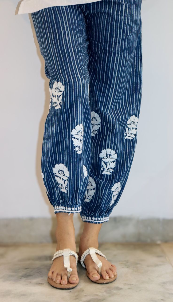 Elevate your style effortlessly with our Pure Cotton Block Printed Stripe Pant in a mesmerizing indigo hue. The perfect blend of tradition and contemporary flair, these pants feature eye-catching Chikankari embroidery in enchanting flower motifs. Crafted from pure cotton, these pants provide a luxurious feel against your skin, ensuring comfort all day long. The indigo hue adds a touch of sophistication, while the block-printed stripes infuse a modern edge, creating a harmonious fusion of timeless elegance and current trends. The highlight of these pants lies in the exquisite Chikankari embroidery that graces them. Delicate flower motifs add a charming and feminine touch, making these pants a standout piece in your wardrobe. Whether you're headed for a casual outing or a special occasion, t Indigo Bohemian Relaxed Fit Bottoms, Summer Indigo Cotton Pants, Summer Cotton Pants In Indigo, Indigo Cotton Pants For Summer, Traditional Embroidered Ankle-length Bottoms, Spring Cotton Indigo Pants, Indigo Cotton Pants With Elastic Waistband, Summer Cotton Pants With Chikankari Embroidery, Indigo Cotton Straight Pants