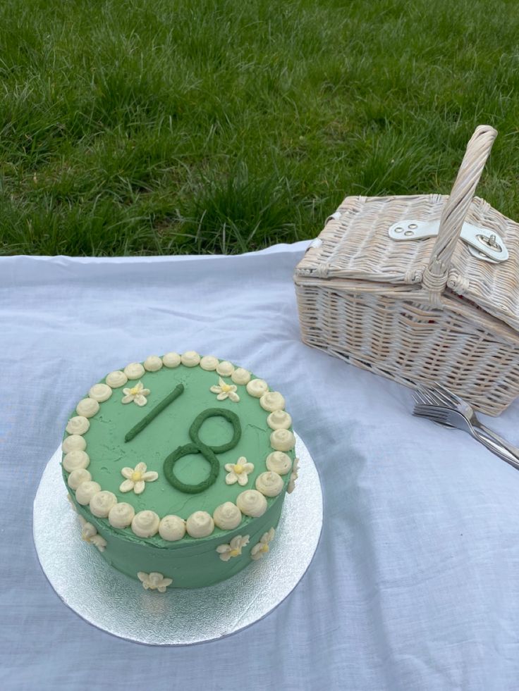 a green cake sitting on top of a table next to a wicker basket and fork