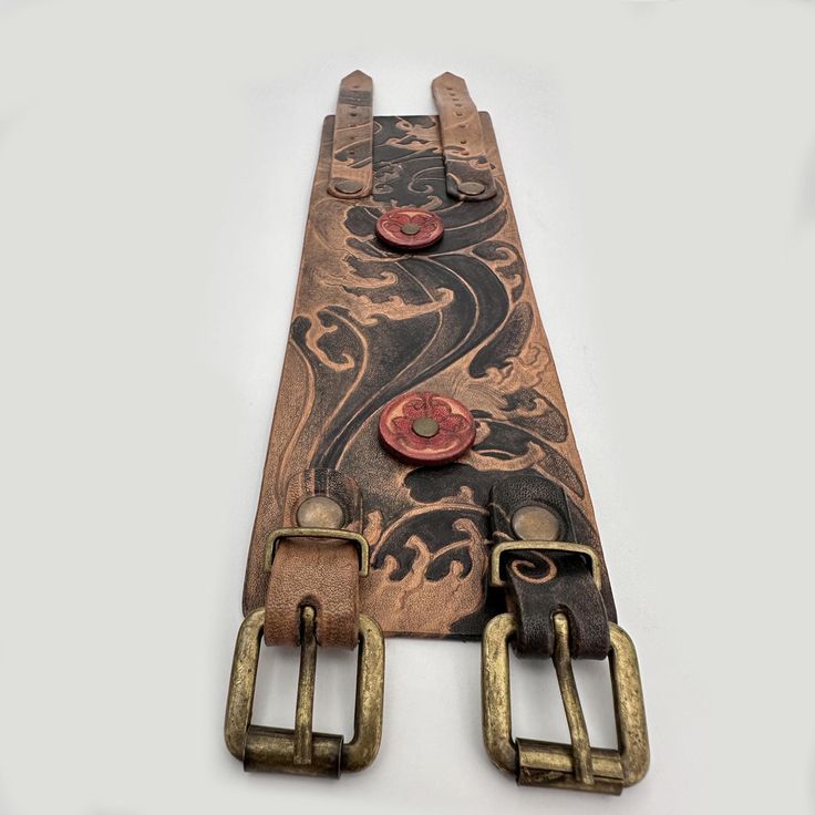 the belt has two metal buckles on it and is decorated with an intricate design