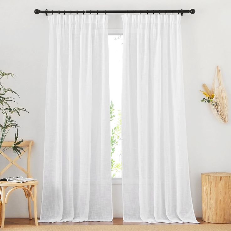 a white curtain hanging on a wall next to a wooden chair and potted plant