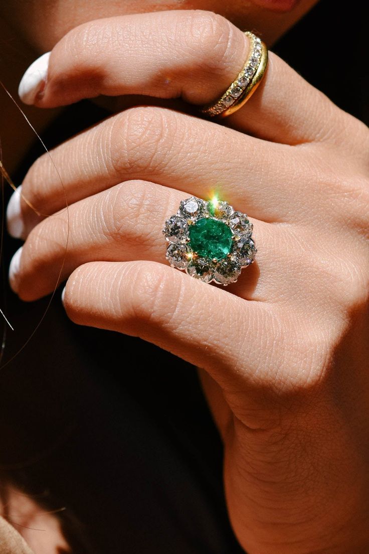 a close up of a person's hand with a ring on their finger and an emerald in the middle