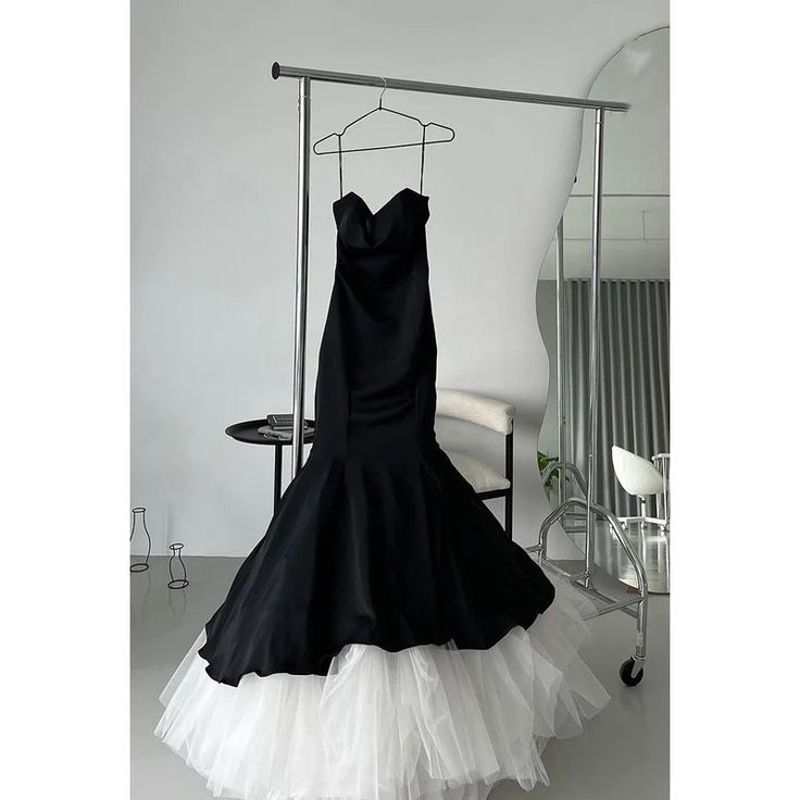 a black and white dress is hanging on a rack in front of a chair with a mirror