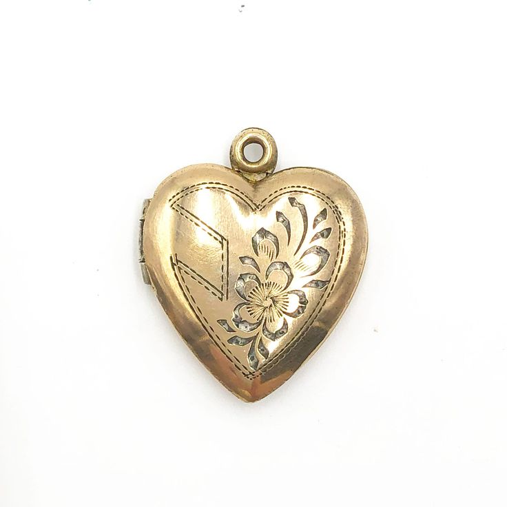 "Vintage Gold Heart Shaped Engraved Photo Locket. The locket is a lovely vintage 12K gold filled over sterling silver heart shaped locket. It has an engraved design on the front of a heart and flower. It snaps shut and contains two frames inside for your photos. The locket is marked 12K on STERLING. This piece is on good vintage condition with slight darkening on the bail where it meets the heart.   15/16\" l x 3/4\" w 3/8\" projection 3 grams Good vintage condition" Vintage Double Heart Engraved Locket Necklace, Vintage Locket Necklace With Heart Charm For Gifting, Vintage Heart Charm Locket Necklace As A Gift, Vintage Brass Locket Necklace For Valentine's Day, Valentine's Day Antique Gold Locket Necklace With Vintage Charm, Vintage Personalized Heart Locket Necklace, Vintage Personalized Locket Necklace For Valentine's Day, Personalized Vintage Heart Locket Necklace, Heirloom Engraved Locket Necklace For Valentine's Day