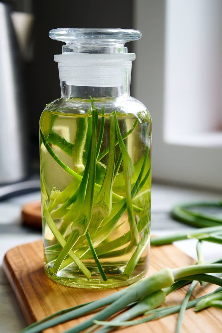 a glass bottle filled with green tea sitting on top of a wooden cutting board