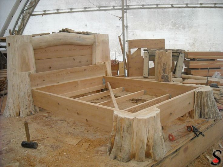 an unfinished bed frame sitting in the middle of a room filled with wood planks