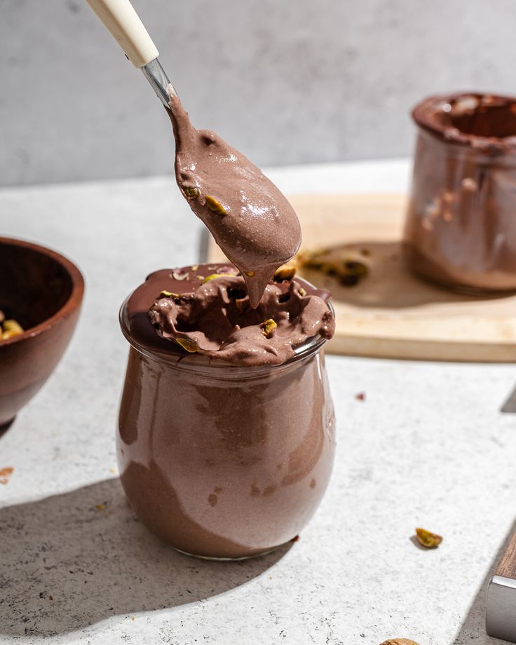 a spoon full of chocolate pudding with nuts on the side