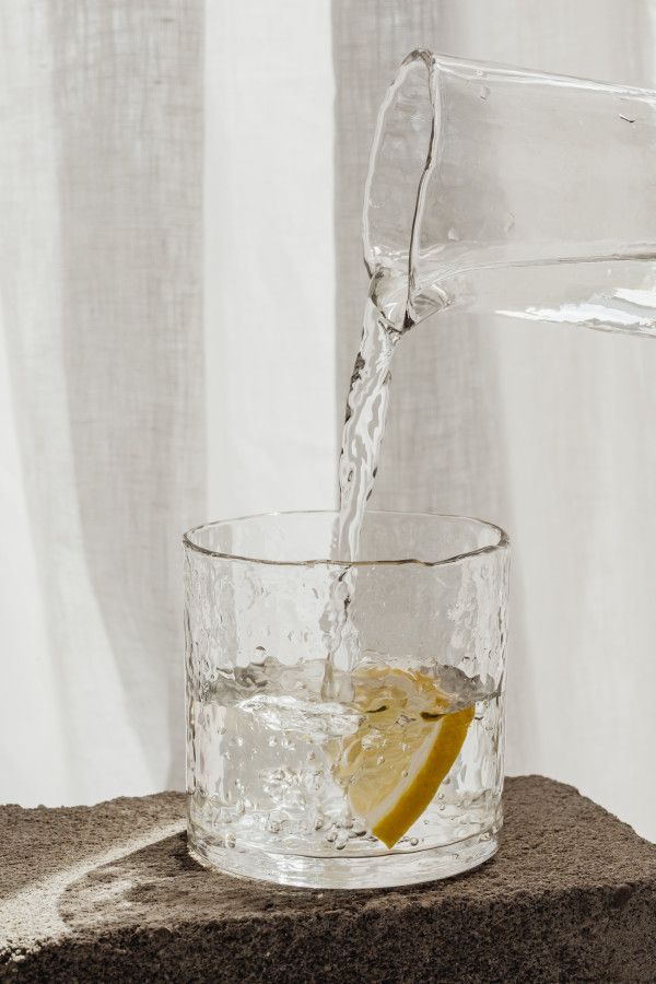 a pitcher pouring water into a glass filled with lemon wedges