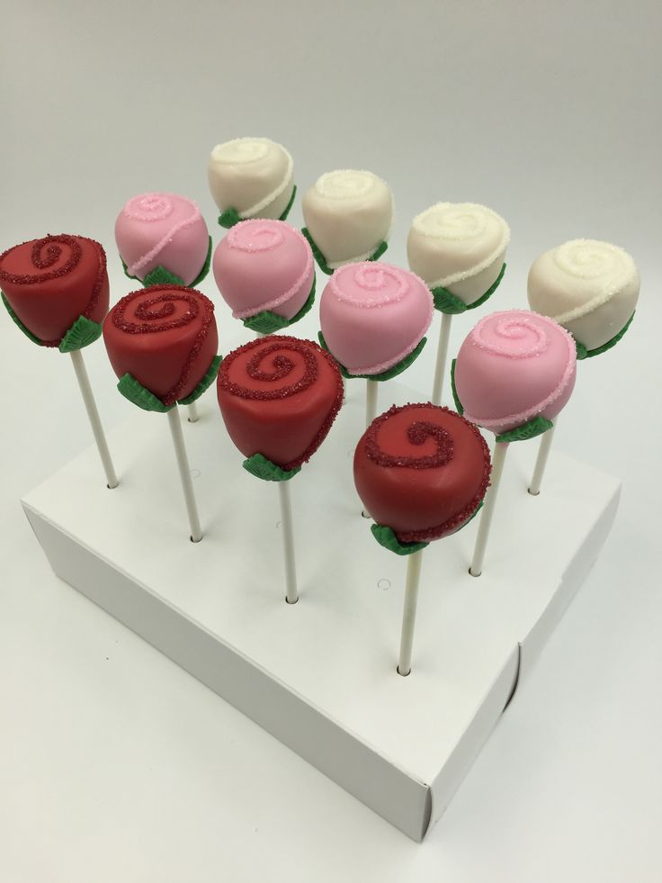 there are many cake pops on the white stand with red and pink frosting in them