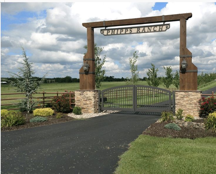 a gated entrance to a grassy field with trees and flowers in the foreground