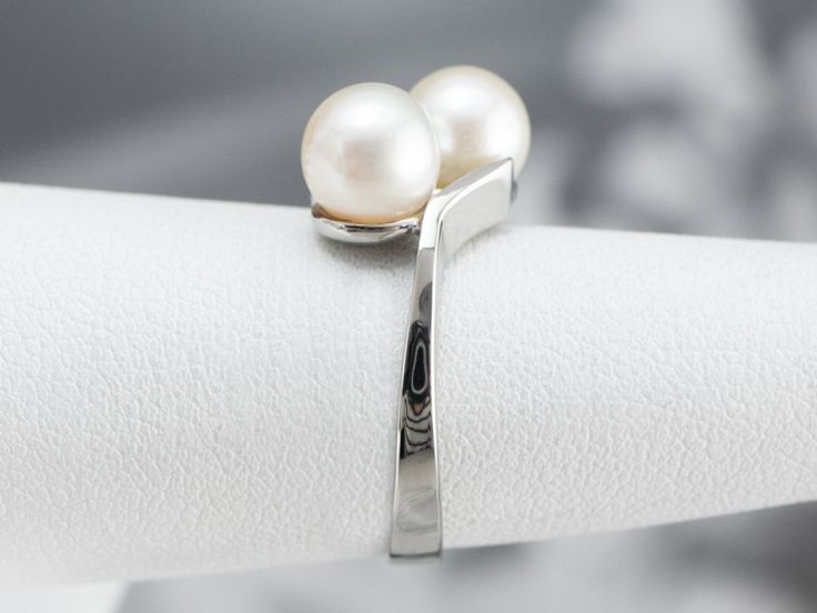 This luxurious pearl ring has a classical bypass style that is timeless! The pearls sit in the center of curving, polished heads with perfectly proportioned prongs. Easy to wear day or night, this pretty pearl ring is classic and timeless. Metal: 10K White Gold Gem: 2 Pearls Gem Measurements: 6.4 mm, Round Ring Size: 6 Marks: "10K" Stamped on the inside band Formal Pearl White Open Pearl Ring, Formal Pearl White Open Ring, Classic White Bypass Ring For Formal Occasions, Formal White Open Bypass Ring, Elegant White Bypass Open Ring, Elegant White Open Bypass Ring, White Gold Pearl Ring, Aquamarine Cocktail Ring, White Pearl Ring