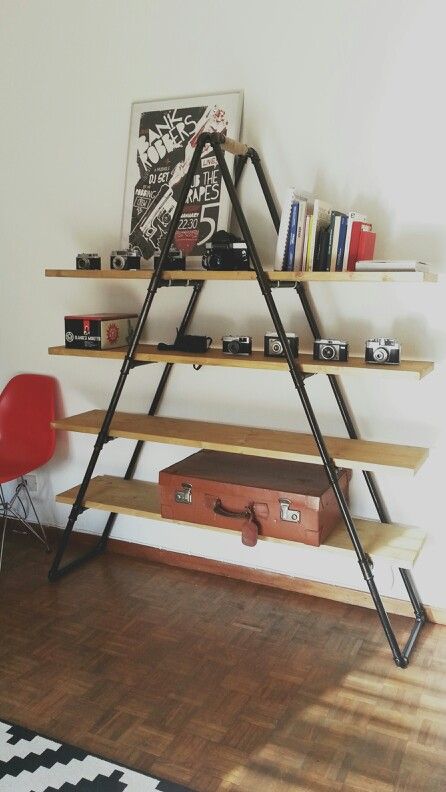 a ladder shelf with books and other items on it in a room next to a red chair