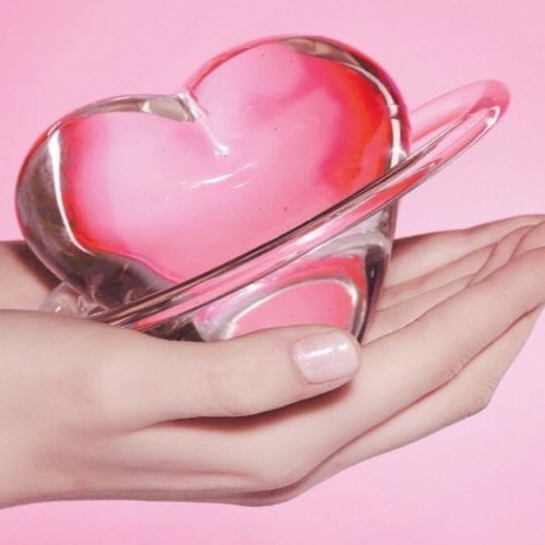 a woman's hand holding a pink heart shaped object in front of a pink background