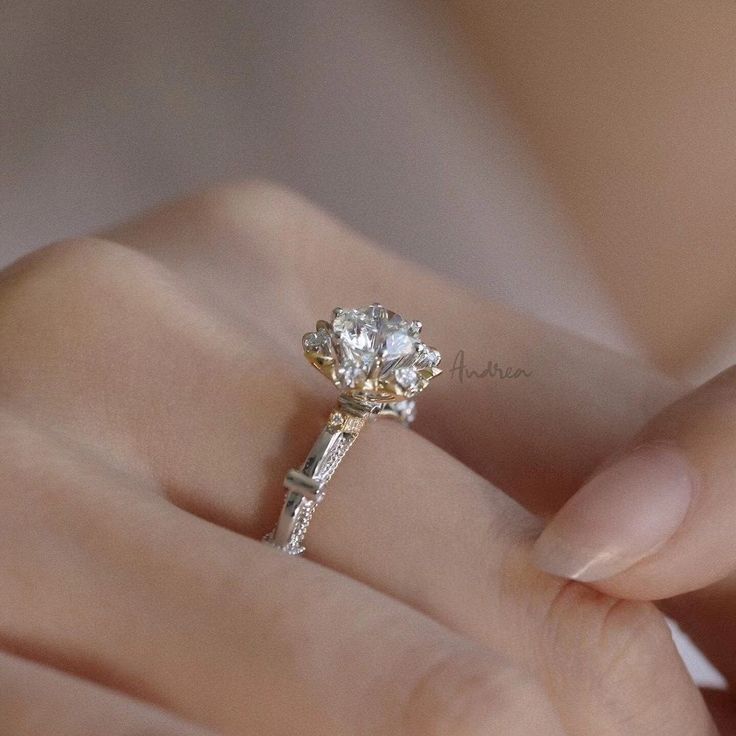 a woman's hand holding an engagement ring with a flower design on the side