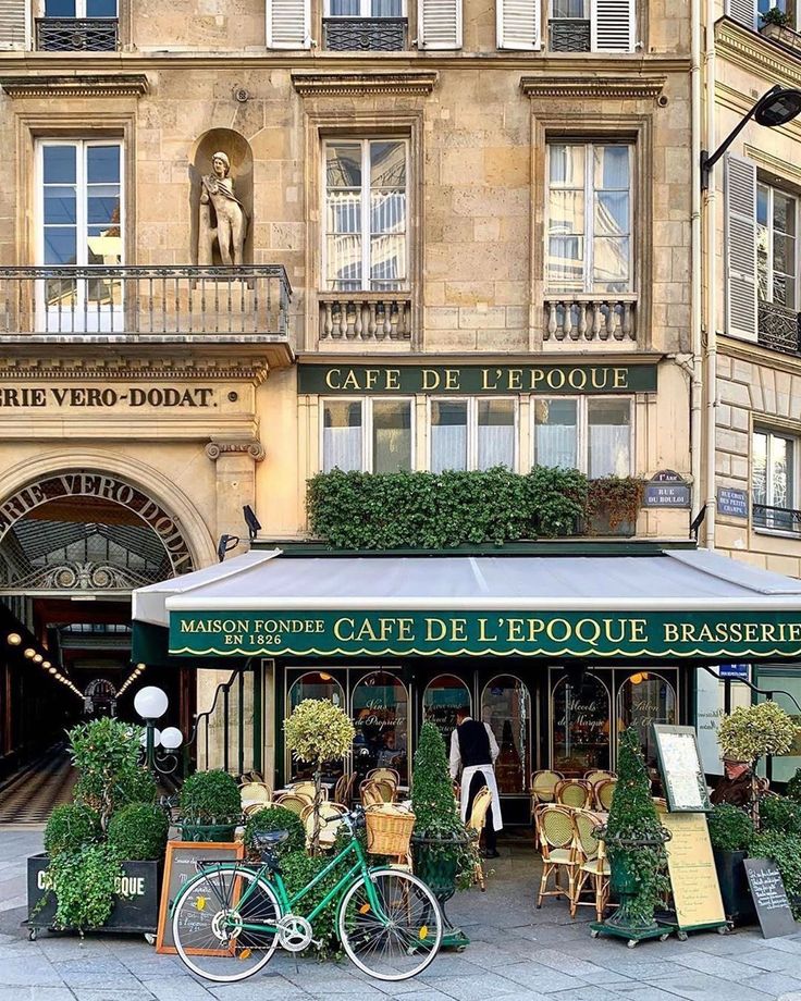 a green bicycle parked in front of a cafe with potted plants on the outside