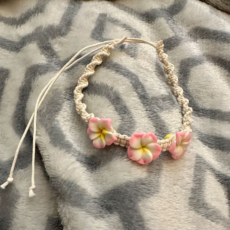 a bracelet with pink and yellow flowers sitting on top of a gray blanket next to a white string