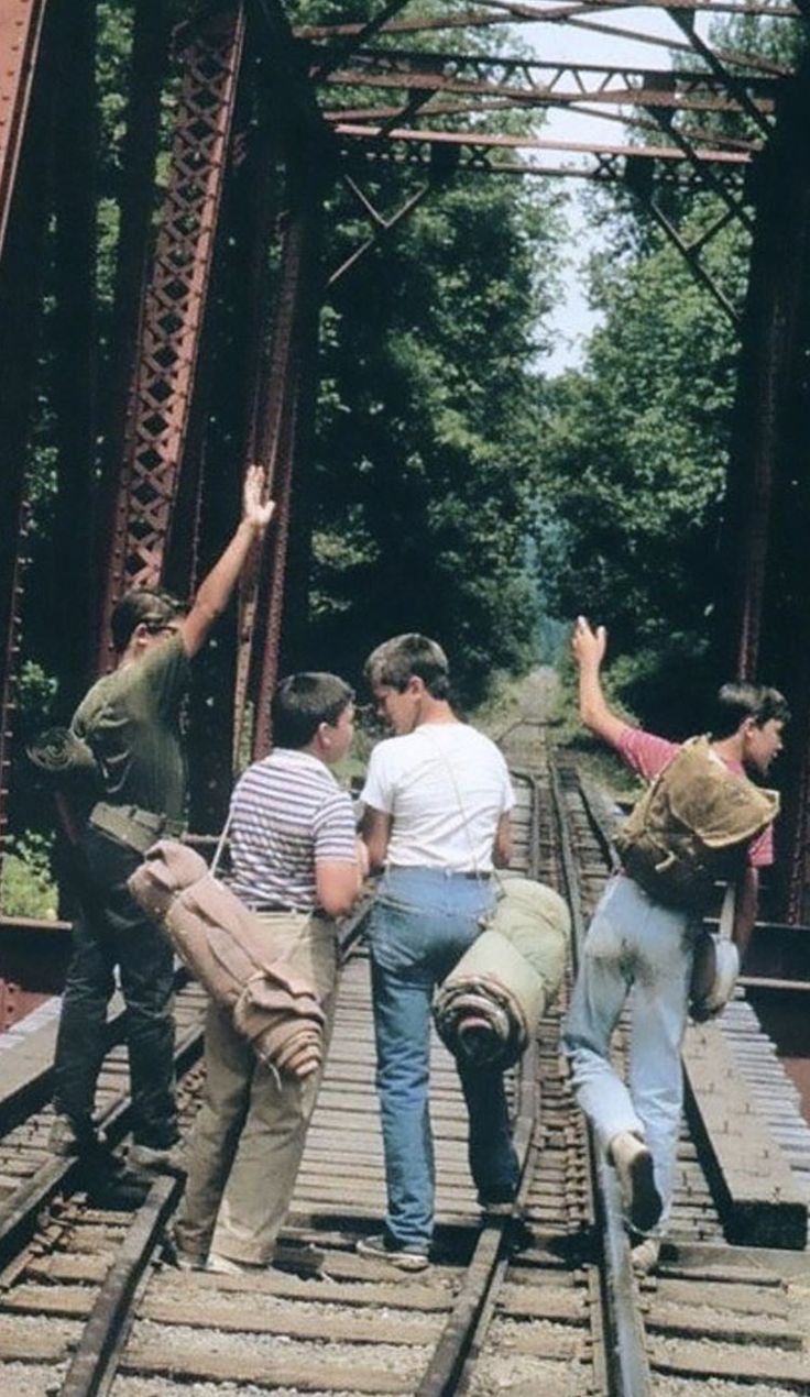 four men walking across a bridge with backpacks on their backs and arms in the air