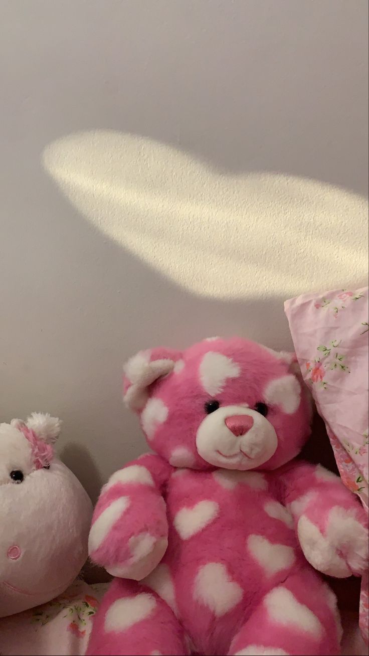 two teddy bears sitting next to each other on a bed with pink and white sheets