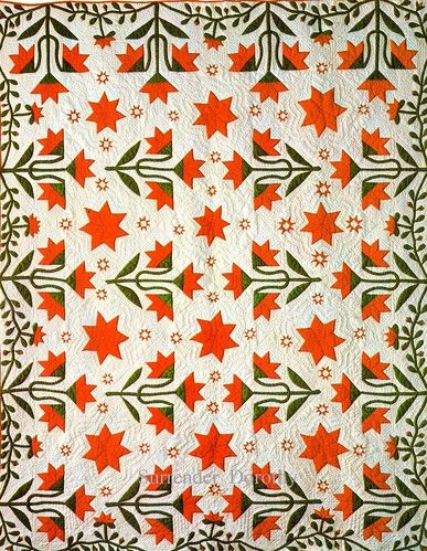 an orange and white quilt with red stars on the front, along with green leaves